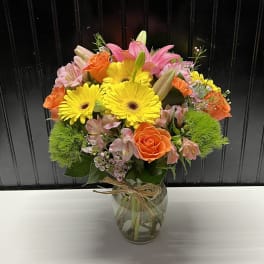 Bouquet of yellow gerbera daisies, orange roses, and pink lilies in a glass vase