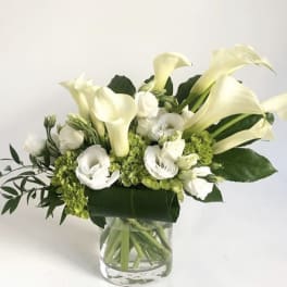 White calla lilies and white blooms arranged in a clear glass vase