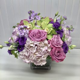 Pink roses and purple flowers arranged in a clear square vase