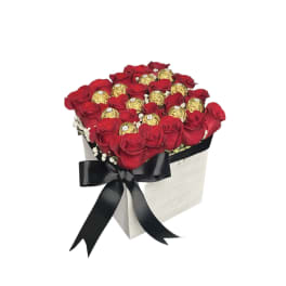 Square box arrangement of red roses and gold-wrapped chocolates with a black ribbon bow