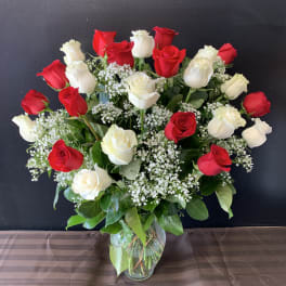 Tall arrangement of red and white roses with tiny white filler flowers in a clear glass vase