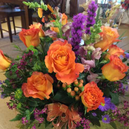 Orange roses and purple flowers in a glass vase with a ribbon