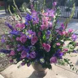 Large purple and pink floral arrangement in a pedestal vase outdoors