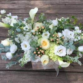 White floral arrangement with calla lilies, roses, and lisianthus in a clear container