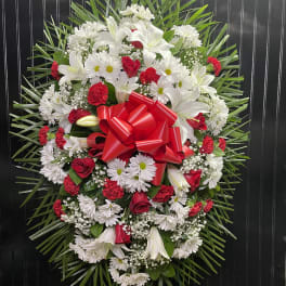 Oval floral wreath with white lilies, daisies, and red roses, finished with a red bow