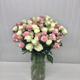 Tall clear vase of light pink and white roses arranged in a full, rounded display