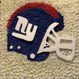Floral tribute in blue, red, and white shaped like a football helmet with the Giants logo