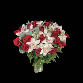 Arrangement of red roses and white cymbidium orchids in a clear glass vase against a black background
