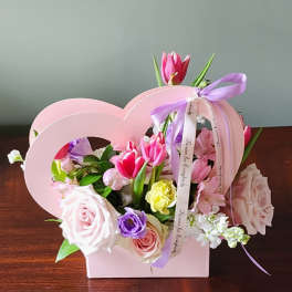 Pink and purple flower arrangement in a heart-shaped box with ribbon