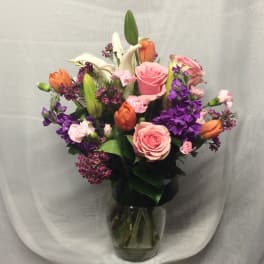 Mixed bouquet of pink roses, orange tulips, white lilies and purple flowers in a clear glass vase