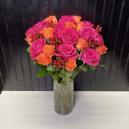 Tall glass vase of hot pink and orange roses with red berries in a rounded bouquet