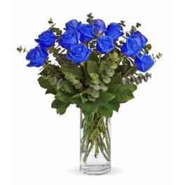 Arrangement of bright blue roses with eucalyptus in a clear glass cylinder vase