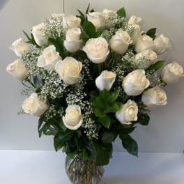 Tall arrangement of white roses with baby's breath in a clear glass vase