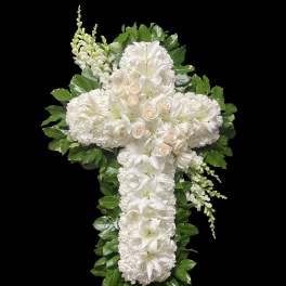 White floral cross arrangement with lilies and roses on a black background