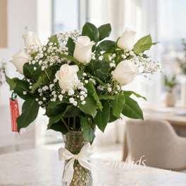 White roses and baby's breath in a clear glass vase with a ribbon