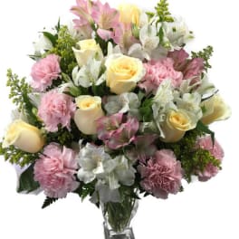 Bouquet of pink and white flowers with pale yellow roses in a clear glass vase
