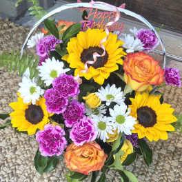 Mixed bouquet with sunflowers, roses, daisies, and carnations under a Happy Birthday topper