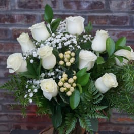 White roses arranged with baby's breath and greenery in a vase