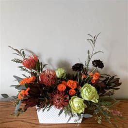 Orange and green floral arrangement in a white rectangular container