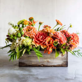 Orange and coral flowers arranged in a rustic wooden box