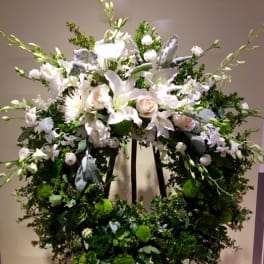 Large white floral wreath on an easel with roses and lilies
