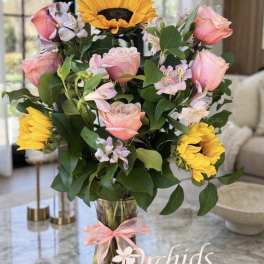Pink roses and yellow sunflowers in a glass vase with a pink ribbon