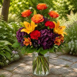 Bouquet of orange roses, yellow lilies, and purple hydrangeas in a glass vase