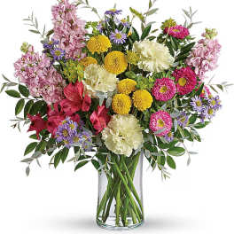 Mixed bouquet of pink, yellow, white, and purple flowers in a clear glass vase