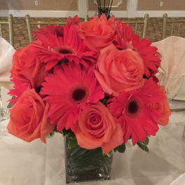 Pink and coral roses with hot pink gerbera daisies in a clear square vase
