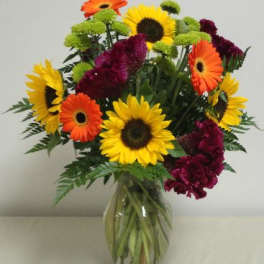 Bouquet of sunflowers, gerbera daisies, and burgundy flowers in a glass vase