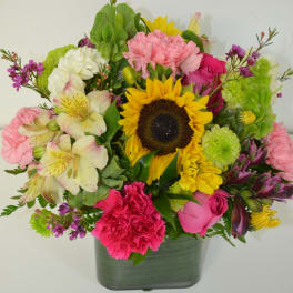 Mixed bouquet with a sunflower, pink carnations, and roses in a glass vase