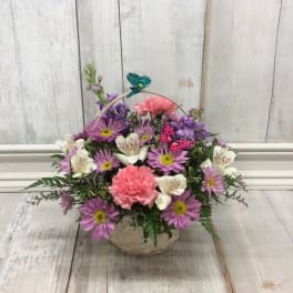 Basket arrangement of pink and purple flowers with a butterfly pick
