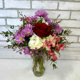 Mixed bouquet of red, pink, purple, and white flowers in a clear glass vase