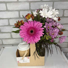 Mixed bouquet with bright pink gerbera daisy in glass vase next to a to-go coffee cup in a cardboard caddy.