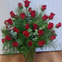 Red roses arranged in a clear glass vase with airy greenery