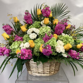 Basket arrangement with yellow roses, white roses, pink flowers, and green hydrangeas