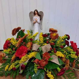 Angel figurine above a low floral arrangement with red and yellow blooms