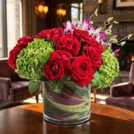 Red roses and green hydrangeas in a glass vase with purple orchids