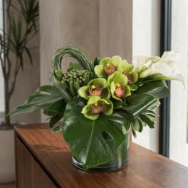 Green orchids and white calla lilies arranged in a glass vase