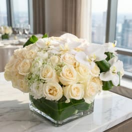 Cream rose and white orchid arrangement in a square glass vase