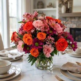 Bouquet of orange roses, pink carnations, and purple daisies in a glass vase