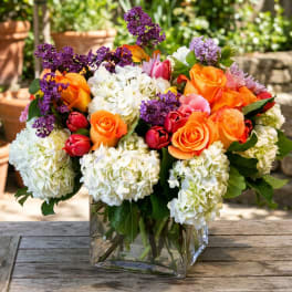 Bouquet of orange roses, white hydrangeas, and purple flowers in a glass vase