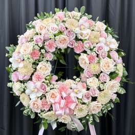 Large pink and cream floral wreath on a stand with a pink ribbon bow