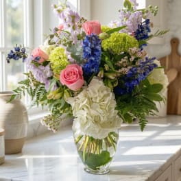 Mixed bouquet of pink roses, white hydrangea, and blue flowers in a glass vase