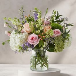 Mixed pastel bouquet of roses, hydrangea, and purple flowers in a glass vase