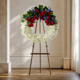 Floral wreath on an easel with red roses, white flowers, and blue accents