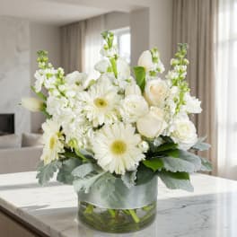 White floral arrangement in a glass vase with a pale ribbon wrap
