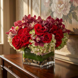 Red roses and purple orchids arranged in a clear square vase