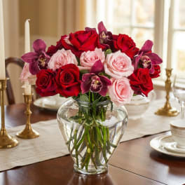 Red and pink roses with purple orchids in a clear glass vase