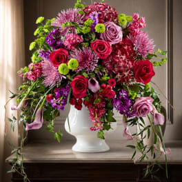 Large mixed bouquet of pink, purple, and green flowers in a white vase